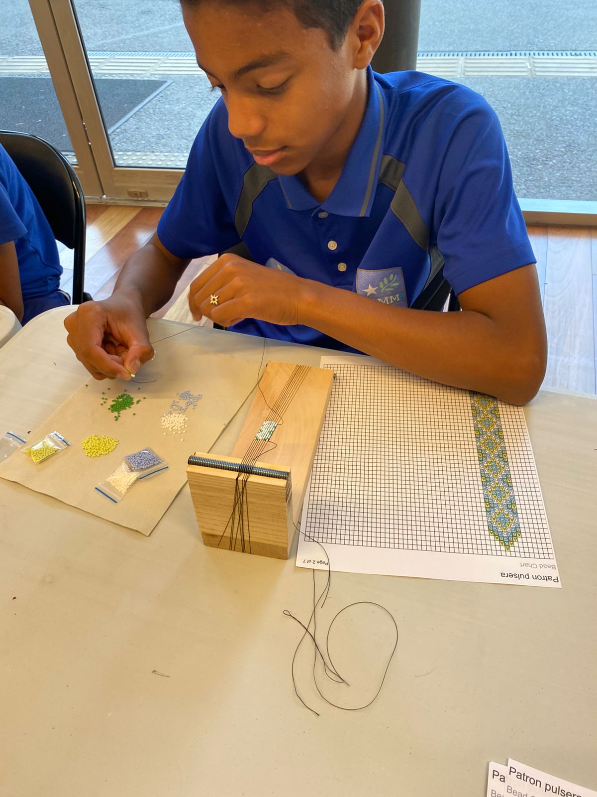 Joven participante de tejido Chakana, siguiendo un patrón ancestral para crear una pulsera.